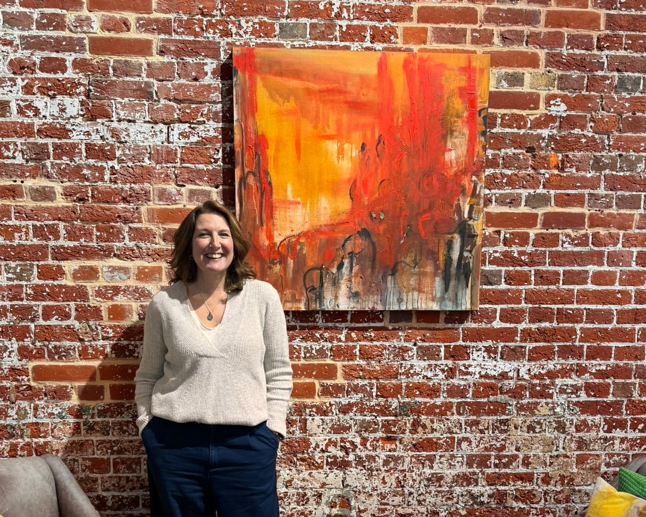 Woman standing in a gallery with a brick wall and colourful red abstract painting